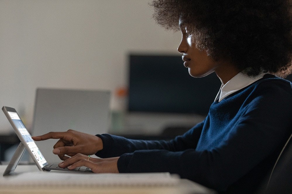 一位女士在办公桌前触摸 Surface Go 2 屏幕，专注工作