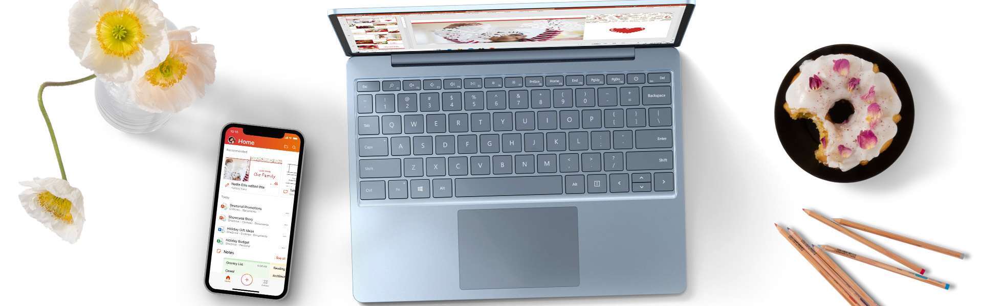 桌上摆放着 Surface Laptop Go、手机、鲜花和一盘甜甜圈