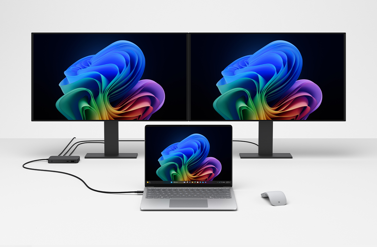 Surface USB4 扩展坞正在为一台 Surface 笔记本电脑充电，它还能在后台将笔记本电脑与两台显示器连接起来。 