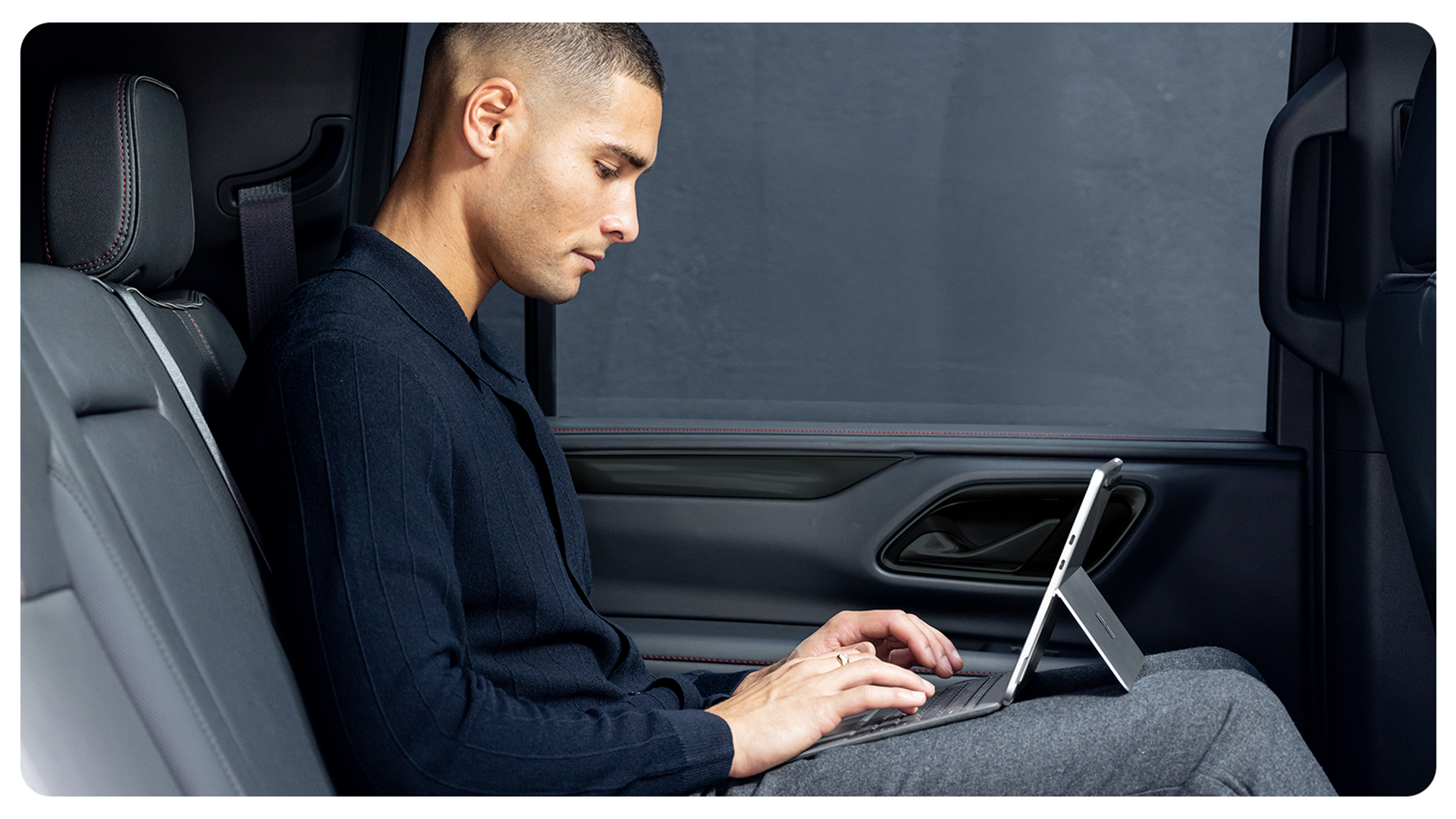一个人坐在汽车后座，展开一体式支架使用 Surface Pro 商用版，显示出该设备的灵活性与便携性。